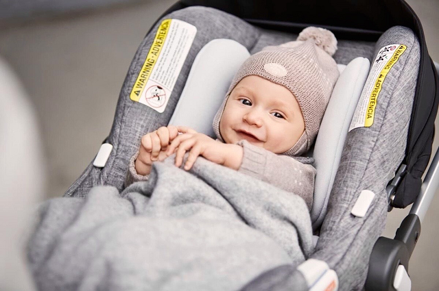 Los mejores asientos de automóvil para el 2021, baby boy dressed in winter clothes and covered in a blanket, sitting in a gray car seat.